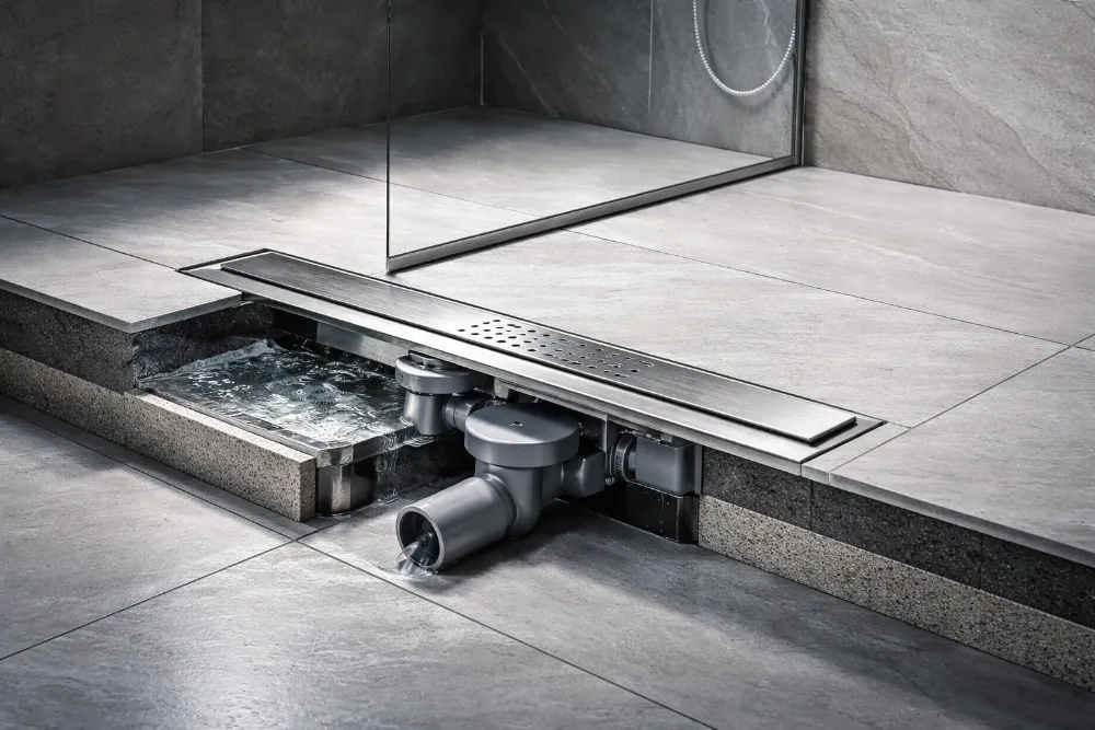 Вбудований лінійний душовий трап у підлозі душу з ухилом плитки та показаною системою водовідведення